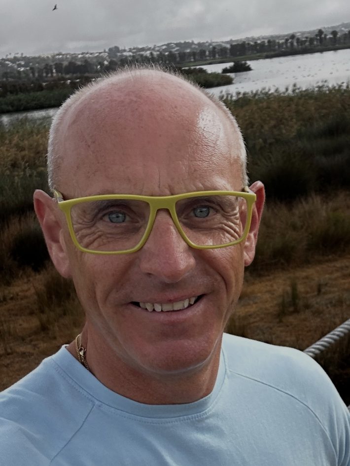 Portrait of Kieran O’Toole outdoors beside a waterside landscape.