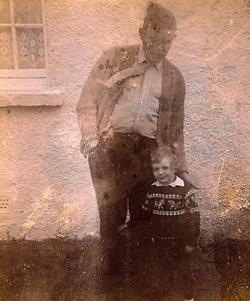 Old family photograph of a man standing outdoors beside a young boy.