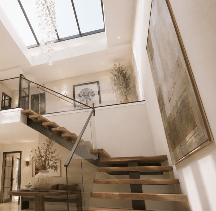 Architectural visualisation by Heron & Moss of a contemporary double-height interior with an open timber staircase, glass balustrade and rooflights.
