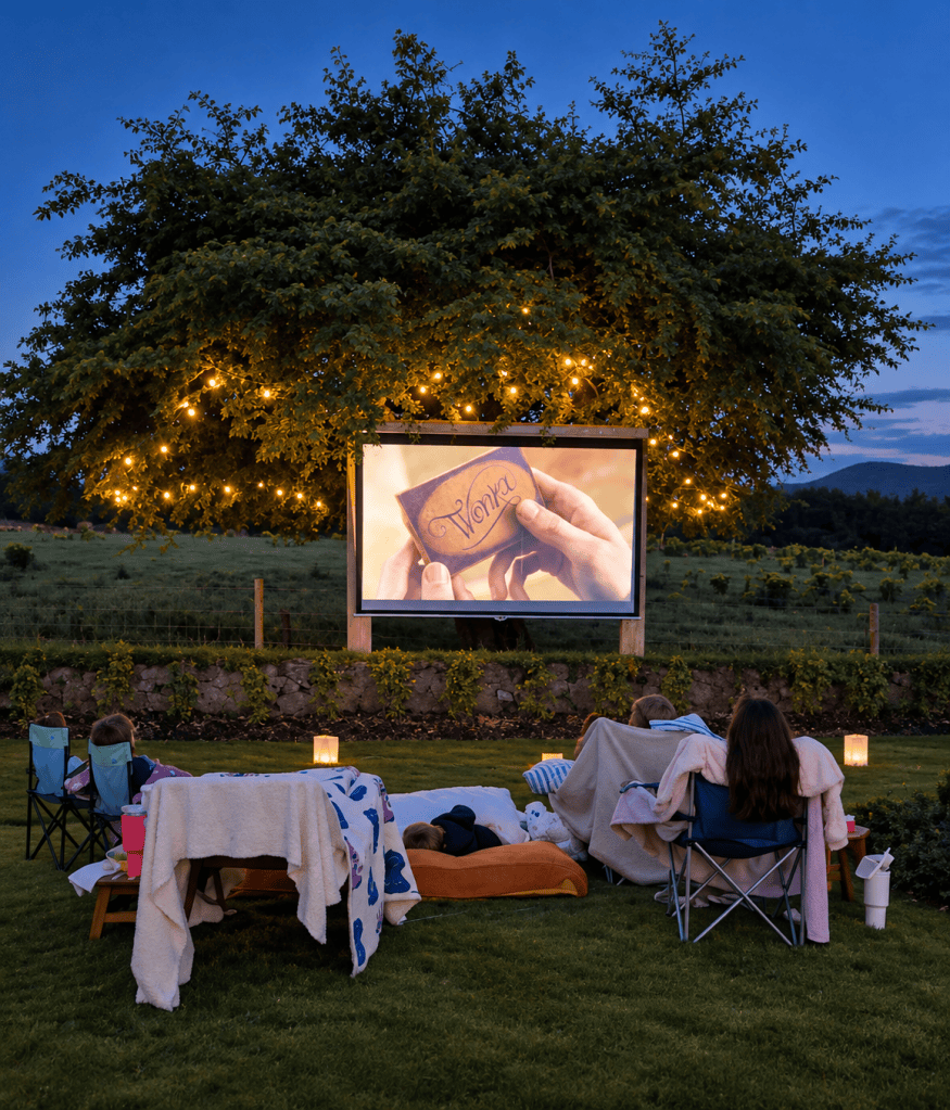 Outdoor screening of Wonka beneath the fairy-lit hawthorn at Hatfield House, with chairs and blankets arranged on the lawn.